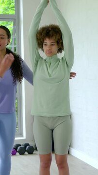 Vertical video: Touching coach aligning client in green on purple mat, home gym, phone on tripod