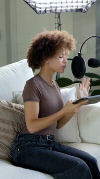 Vertical video: Sitting woman in brown tee with tablet, adjusting mic, recording in home studio