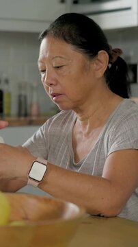 Vertical video: Looking, senior woman reading label before sipping glass at table with pink watch