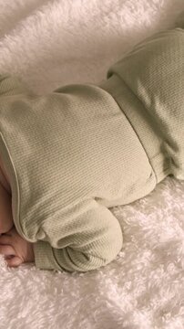 Vertical video: Stirring infant shifting after small shift on plush blanket at home in green onesie