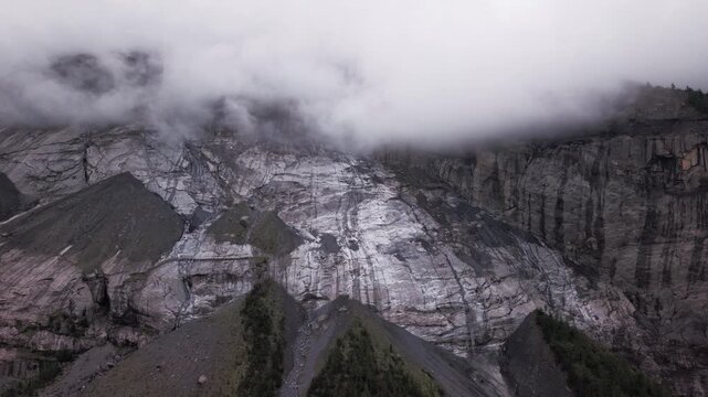 Dramatic aerial view of rocky glacier peak shrouded in thick white fog and clouds