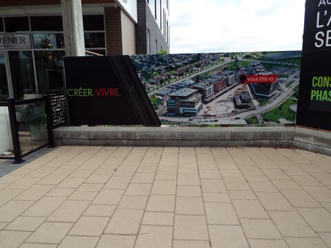 Gatineau, Quebec, Canada &ndash; May 12, 2026: A construction hoarding displays an aerial site plan with the text "CR&Eacute;ER. VIVRE." and a "VOUS &Ecirc;TES ICI" marker on All&eacute;e de Hambourg Local 138.