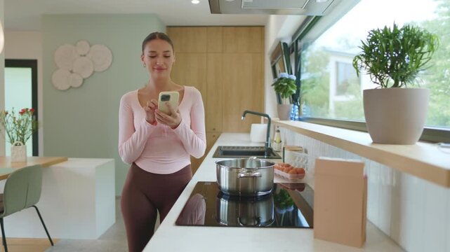 Woman preparing meal at home, looking into saucepan to check cooking process and continue using her smartphone with smile, 4K, cinematic footage