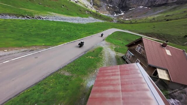 Dynamic FPV drone tracking shot of motorbikes riding through scenic green alpine mountain valley