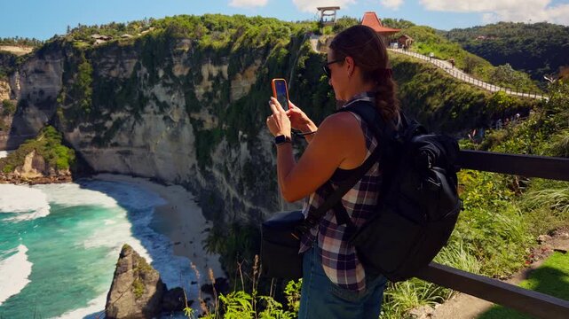 Female Traveler Photographing Diamond Beach from a Scenic Cliffside Viewpoint on Nusa Penida During a Sunny Day