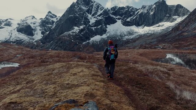 Solo hiker crossing tundra toward snow capped jagged mountain peaks