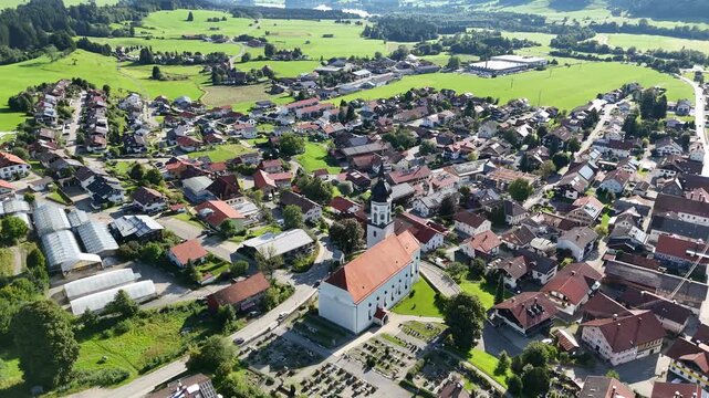 Panorama flight over parish church St. Ulrich in village Wertach with houses and meadows in Allg&auml;u Alps, Bavaria, Germany