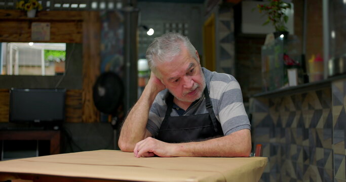 Concerned small business owner sits alone at table showing despair uncertainty and emotional weight of struggling to sustain neighborhood caf&eacute; during hard economic times