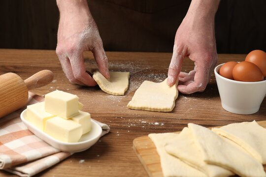 Man with raw puff pastry dough at wooden table, closeup
