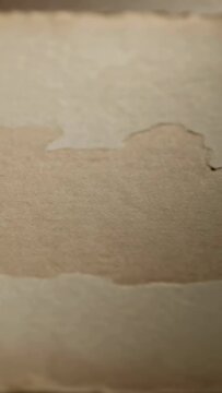 Vertical video: Panning camera revealing spreading brown stain on textured paper at desk, dark edge