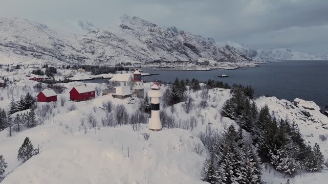 Aerial winter view of coastal village with white lighthouse and snowy pine trees