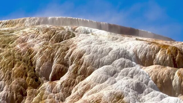 Mountain of mineral deposits with overflowing water from the hot springs with steam rising above the falling water
