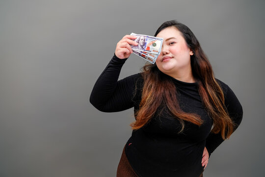 Woman holds money near eyes, smiling mischievously