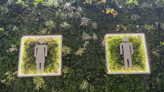 Modern public restroom signs with man and woman icons on plant wall