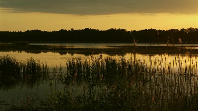 wieczorny widok na spokojną taflę jeziora na tle zachodzącego słońca w ciepłych barwach