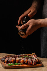 Obraz premium Chef seasoning sliced porterhouse steak with pepper on wooden serving board