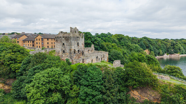Scenic view of the medieval Ravenscraig Castle ruins on a rocky cliff surrounded by lush green trees and coastline in Fife, Scotland