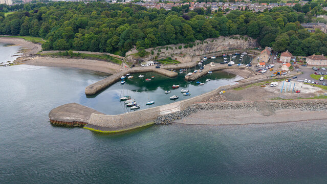 Aerial view of the historic Dysart Harbour with boats, stone piers, and scenic coastline in Fife, Scotland.