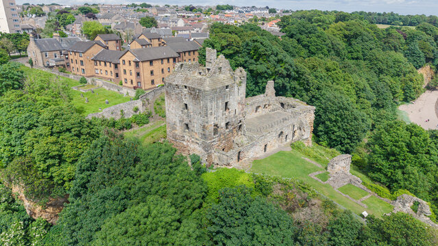 Scenic view of the ruined historic Ravenscraig Castle fortress surrounded by green trees and traditional houses in Fife, Scotland.