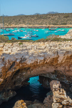 Natural rock arch of Pont natural d'Es Cal&oacute; Blanc overlooking turquoise bay with boats at Cala Varques, ideal for travel websites