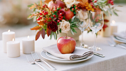 Fototapeta premium Elegant autumn table setting with seasonal floral centerpiece, candles, glassware, and a fresh apple placed on a folded napkin
