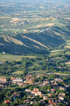 Aerial view of a small village nestled among green hills, fields and wooded countryside in warm evening light.