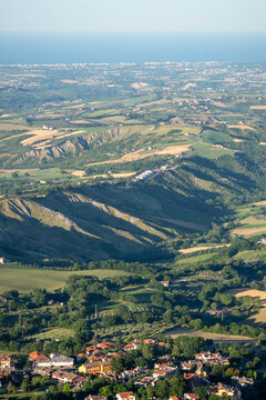Aerial view of a small village nestled among green hills, fields and wooded countryside in warm evening light.