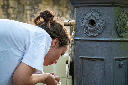 young woman drinking water from a street fountain