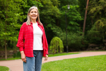 Fototapeta premium Beautiful senior woman walking in spring park, space for text