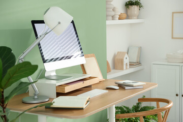Fototapeta premium Workplace with computer monitor on riser stand, lamp and stationery indoors