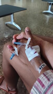 A close up of two people holding hands in a healthcare setting while one receives medical treatment with an intravenous line in place, representing emotional support, patient care, and human connectio