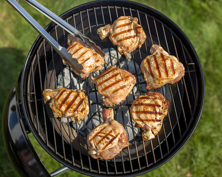 Grilled chicken thighs cooking on charcoal barbecue grill top down view summer outdoor meal