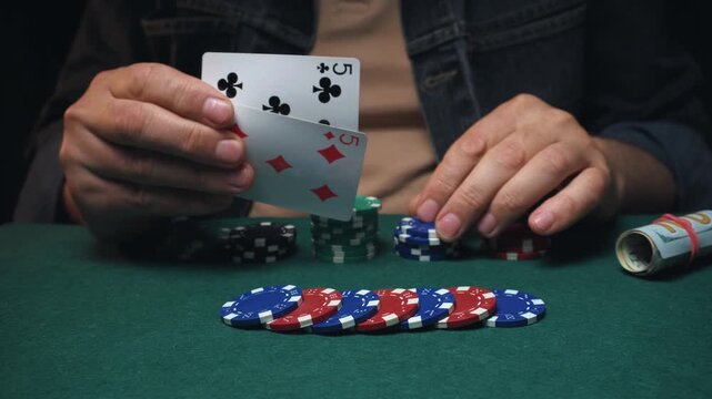 Individual with light skin playing poker reveals cards while seated at a green felt table surrounded by colorful poker chips and a beverage can