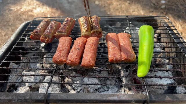Traditional Turkish Tekirdag meatballs and green pepper cooking on hot outdoor charcoal grill during backyard barbecue picnic.