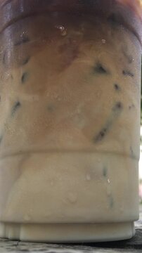 Close up, stirring and mixing an iced latte until the milk has combined with the coffee. 
