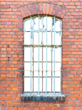 An old window with metal bars in a red brick building with broken windows. The building's interior is isolated.