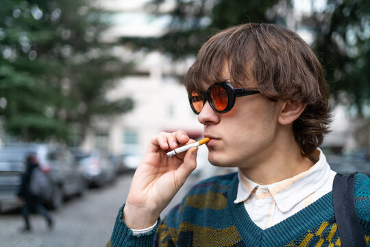 Gen Z retro fashion young man smoking cigarette on city street, hipster sunglasses, youth lifestyle, addiction concept.