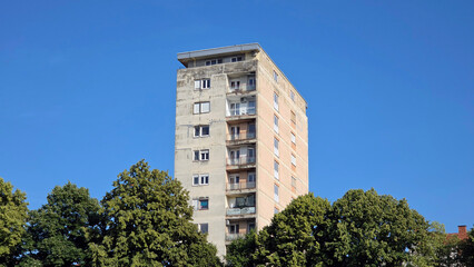 High angle view of a tall residential concrete apartment block behind green trees © hecos