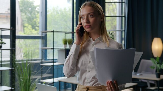 Caucasian businesswoman excited satisfied with documents talking mobile phone business woman communicate call about papers female girl with paperwork feeling carefree joyful happy smiling in office