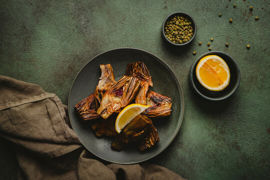 Savory fried artichoke hearts with yellow citrus slice on dark textured surface. Wholesome vegetarian meal preparation and professional culinary recipe concept, horizontal top view.