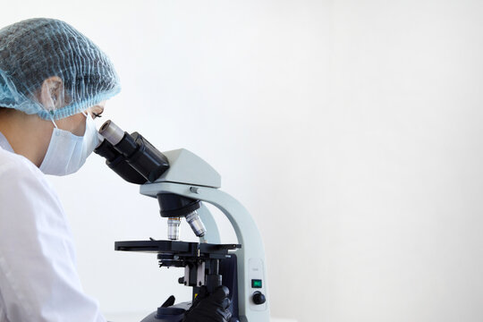 Female scientist looking through microscope in modern chemical laboratory doing some research. Analyzing samples using a microscope on white background with copy space