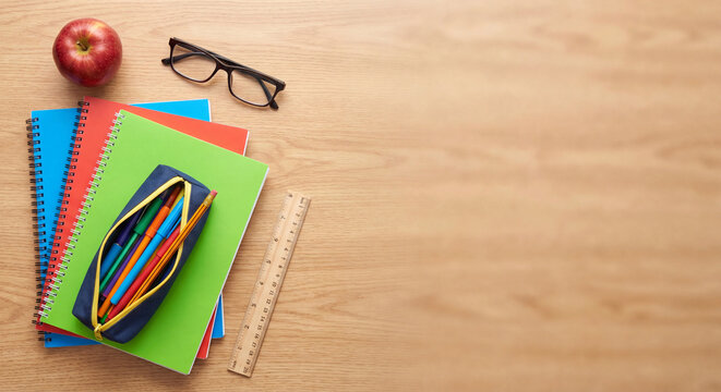 Top view of bright colorful notebooks with a pencil case glasses apple and ruler arranged on a wooden table surface