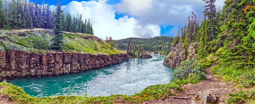 Panoramic view of the nice cloudscape, blue sky, lush vegetation around the river near the canyon. Yukon river flows through the Miles Canyon. Whitehorse, YT, Canada
