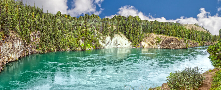 Bright afternoon with clouds and vegetation around the river.. The river will make a 3,500 KM journey to Bering sea from here. Yukon river flows through the Miles Canyon. Whitehorse, YT, Canada