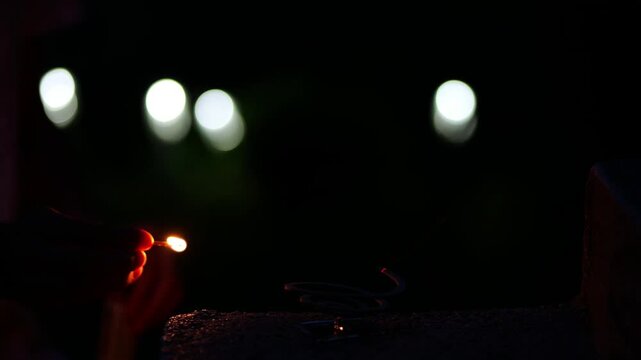 Person lighting a mosquito repellent coil with a match at night