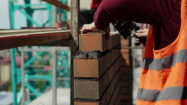 Worker laying brick on corner of masonry wall during construction