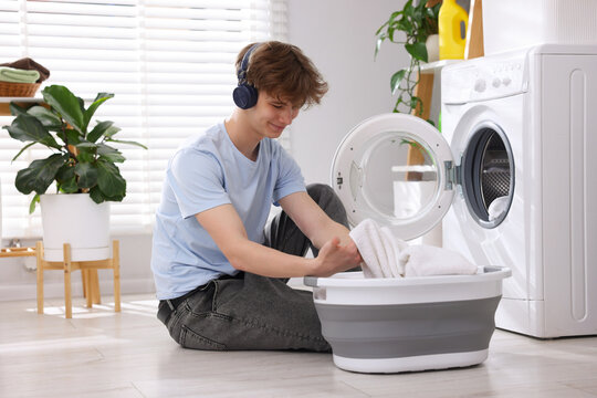 Housework. Teenage boy in headphones with basket doing laundry at home