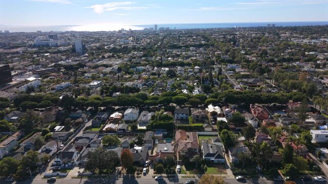 Aerial panorama of Los Angeles California suburban blocks stretching toward ocean horizon, mix of tree pockets, commercial lowrise and residential lots, light shimmer on water and clear atmospheric