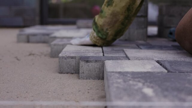 Worker laying concrete paving blocks on prepared sand base