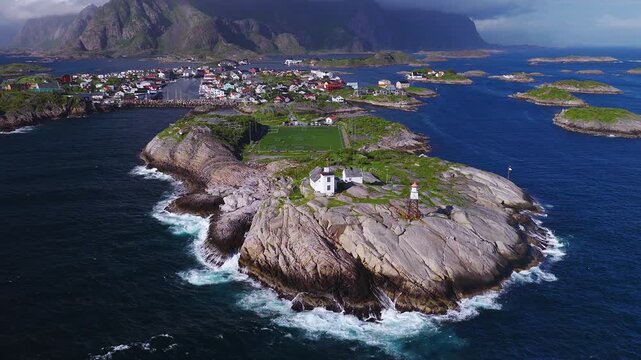 Aerial summer view of Henningsvaer, Lofoten, Norway. Drone moves over the football stadium, stockfish racks, colorful houses, skerries, surf, and steep mountains.